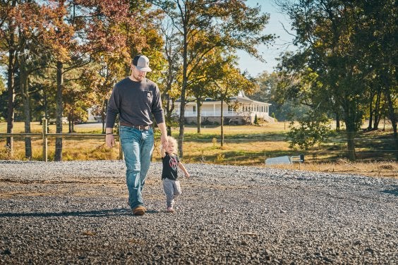 Father and daughter walking on gravel pathway on rural land